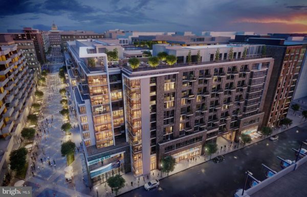 A modern multi-story apartment complex with rooftop greenery and lit windows overlooks a vibrant, tree-lined pedestrian street at dusk.