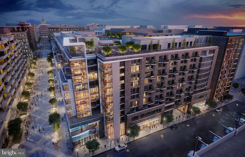 A modern multi-story apartment complex with rooftop greenery and lit windows overlooks a vibrant, tree-lined pedestrian street at dusk.